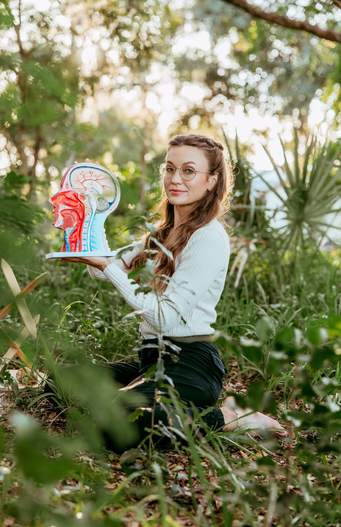 Brooke McPoyle, founder of Musical Breathwork, sitting in a garden holding an anatomical model of the human head